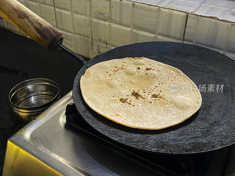 特写图像的roti /薄饼烹饪铸铁塔瓦(扁平，圆形的烹饪锅)，厨房炉燃气燃烧器，全麦atta面粉，高视图，重点在前景